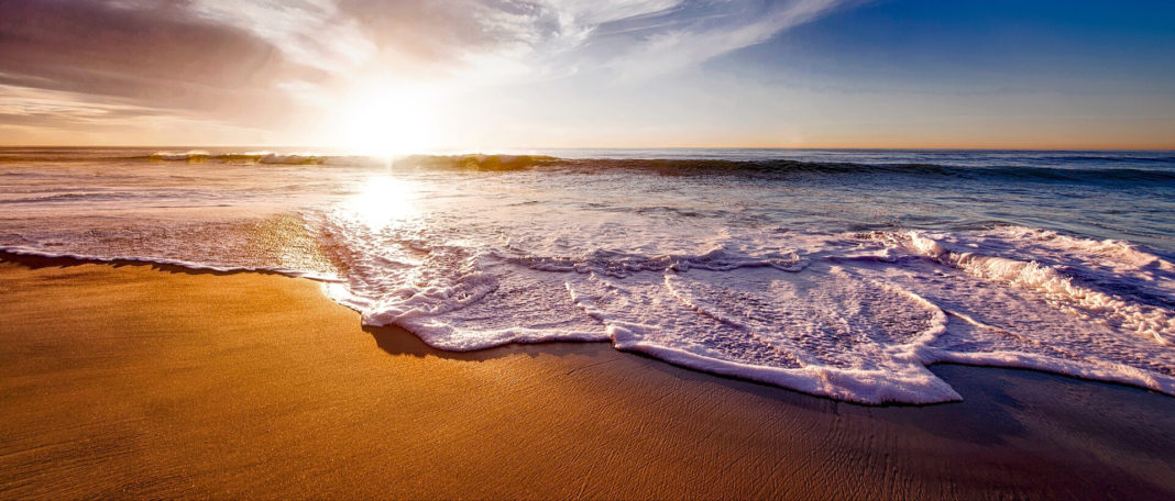 waves crashing on a beach as the sun sets on the horizon